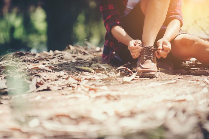 Young woman hiker stops to tie her shoe on a summer hiking trail